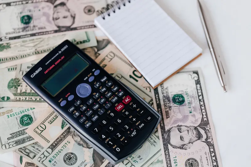 Calculator, notepad, pen and US dollar bills on a white desk