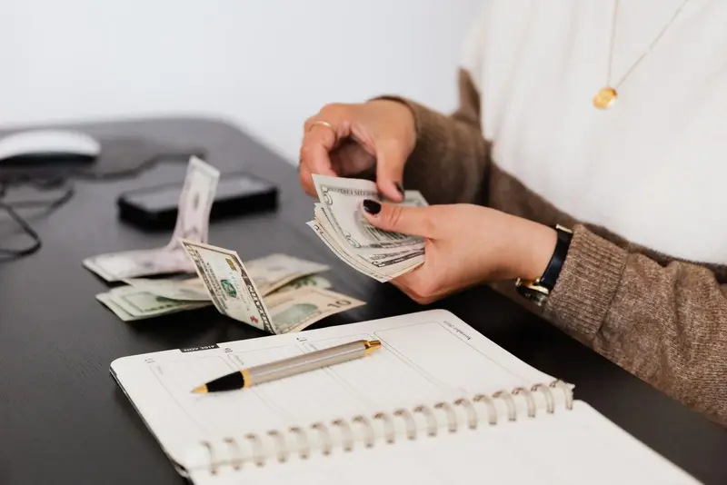 Person counting cash next to an open notebook on a desk